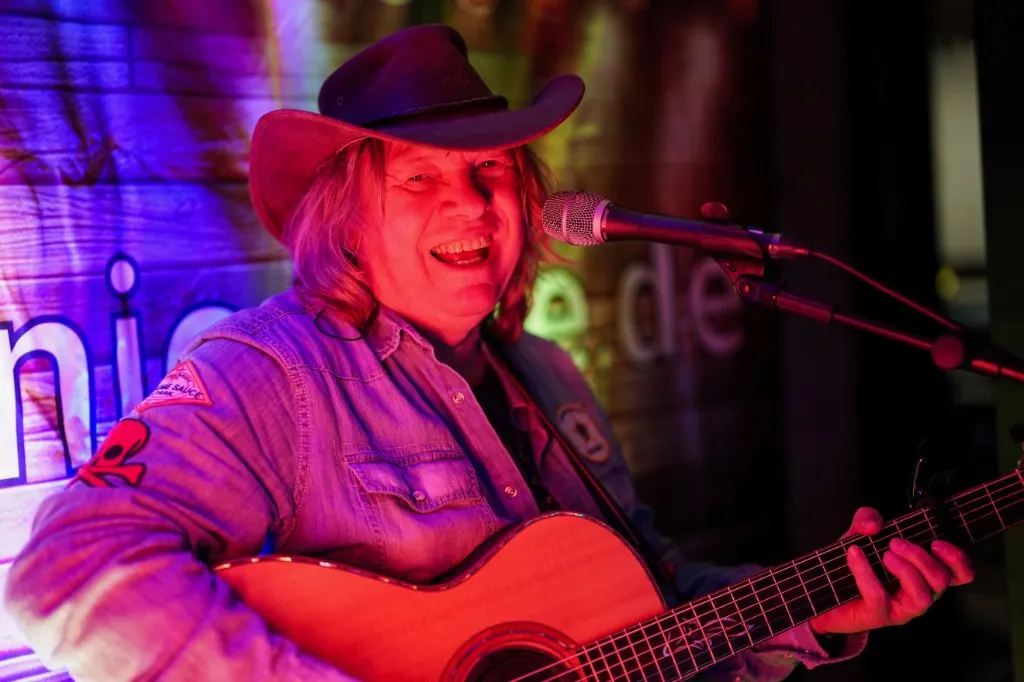 Mannie Live singt ins Mikrofon, Akustikgitarre, farbiges Bühnenlicht