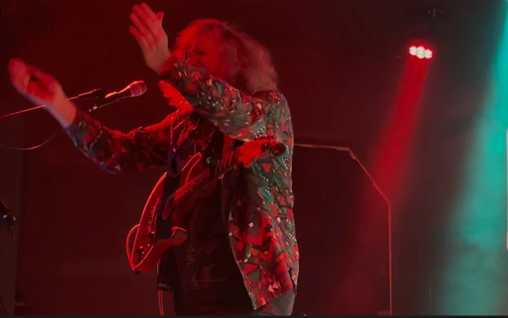 Mannie Live mit roter E-Gitarre auf der Bühne, dramatisches rotes Bühnenlicht